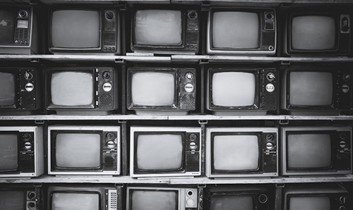 Stacked rows of vintage black-and-white televisions with blank screens, arranged closely on shelves in a monochrome setting.